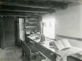 Kila sn, Sala.
Hembygdsgården, interiör av köket med bänk dukat träbord, dörr, bok, tallrikshylla m.m.
