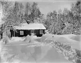 Kloar-Eriks egen stuga i ymnig vinterskrud. Rikligt med istappar hänger längs takskägget.