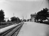 Eskilstuna Södra station, uppförd av Norra Södermanlands Järnväg, NrSlJ. NrSlJ förstatligades 1931 och stationshuset på Eskilstuna Södra station revs av SJ 1936 och byttes ut mot ett mindre.
I bakgrunden syns Fors kyrka.
En man ur personalen tittar ut genom sidodörren på stationshuset. Några barn syns på stationsområdet.