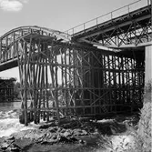 Broarbete vid Skellefteåälven, Kusfors. Järnvägsbron byggdes med en kombination av stående och hängande parabelfackverk. År 1943 hade den ursprungliga bron, som togs i bruk 1893, tjänat ut. Då byttes de tre stålspannen ut mot nya medan samma landfästen och brostöd användes. Den nya bron hade underliggande stålbalkar i alla tre spann. Det långa mittspannet var dessutom utformat som en bågbro med vertikala stag ned till den underliggande balken. Bron trafikerades fram till linjeomläggningen 1993.