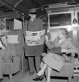 Tågbud säljer tidningar i SJ vagn typ Bo5b. Arrangerad bild. 
En av tidskrifterna i tågbudets väska är Life från 5 september 1949.