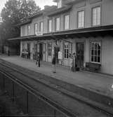 Resande står och väntar på ankommande tåg. Moholms stationshus byggt 1873, tillbyggt 1891.