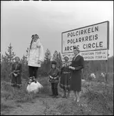 Polcirkeln, kung Bore, Sunlit Nights Land Cruises (SNLC) -värdinna, samer och tomte.
Skylt med texten : 
Polcirkeln
Polarkreis
Arctic Circle
Ekvatorn 7389 km