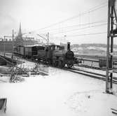 Statens Järnvägar SJ 1856-1956. 100-årsjubileum. Tåg med gamla lok och vagnar vid Tegelbacken på väg mot Stockholm Central, på sträckan mellan Riddarholmen och Stockholm Central. Oxelösund-Flen-Westmanlands Järnväg OFWJ lok 8. .