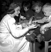 Luciatärnan Berit delar ut julklappar på ett barnhem för föräldralösa barn, Hauptkinderheim in Ruhleben, i utkanten av Berlin i samband med Statens Järnvägars, SJ, luciabesök i Berlin 1958