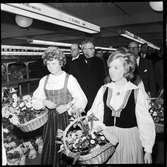 Invigning av Årsta partihandel. Kung Gustav VI Adolf, 2:a från höger bakom kvinnorna i folkdräkt. Kvinnor i folkdräkt med blomsterkorgar