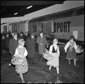 Invigning av Årsta partihandel. Kung Gustav VI Adolf, 2:a från vänster i andra raden. Generaldirektör, Gd, Erik Upmark, 3:a från vänster i andra raden. Kvinnor i folkdräkt med blomsterkorgar
