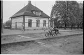 Stationshuset i Åsbo-Össjö. Stationen nedlagd 1953-06-10. Barn med motorcykel på plattformen. Spåren är borttagna.