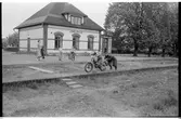 Stationshuset i Åsbo-Össjö. Stationen nedlagd 1953-06-10. Barn med motorcykel på plattformen. Spåren är borttagna.