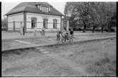 Stationshuset i Åsbo-Össjö. Tågtrafiken upphörde 1953-06-10. Barn leker med motorcykel på plattformen. Spåren är borttagna.