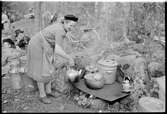 En kvinna kokar kaffe med mera på en platta som är lagd över elden.