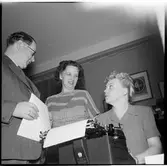 En man och två kvinnor samtalar vid en skrivmaskin.