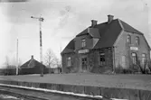 Stationen. Mitt för stationshuset står en semafor med så kallade gallerverksvingar. Signalen visar stopp.