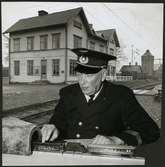 Personal på inklippt bild leker med modelltåg. Stationshuset i Storå i bakgrunden.