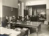 Telegrafexpeditionen Stockholm Central 22/12 1910. Fr.v. vid apparatborden; Stk Malmqvist, Kb Eskil Svensson, Stk Linder, eo Sts Rudolf Skeppstedt, Kb Albihn, ex skrivbitr Zandén, eo Stk Blomberg, Sts Christensson,verkmäst. Santesson, Kb Alb. Carlsten, eo Stk Danielsson, Tlt Ågren,telbud Berggren, Tågledarna vid skrivbordet till vänster är G Dahlström och Nylinder.