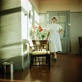 En sjuksyster poserar för Erik vid ett blomsterbord i samband med att han själv opererats. Bland blomstren finns prästkragar, liljekonvaljer och riddarsporre.