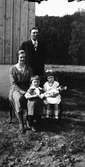 Familjen Henriksson på Lövagård fotograferade vid husknuten. Dottern Maj-Britt håller i en docka, båda har rosett i håret.
