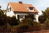 Bostadshus med vit putsad fasad, trappa, takkupa och sadeltak i Skogsliden. Ägaren hette Österberg och byggmästaren var Bertil Danielson.