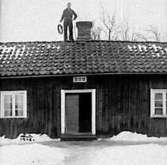 EN SOTARE STÅR VID SKORSTENEN PÅ TAKET HOS ANDERS KARLSSON I HAGEN, GÖTLUNDA. 1948.