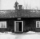 EN SOTARE STÅR VID SKORSTENEN PÅ TAKET HOS ANDERS KARLSSON I HAGEN, GÖTLUNDA. 1948.