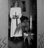 EN KVINNA I VIT KLÄNNING MED LJUSSTAKE I HANDEN