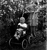 TVÅ SMÅ BARN DEN ENA SITTER I EN KÄRRA