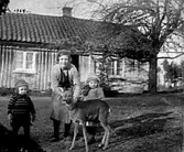 EN MAMMA MED SINA TVÅ BARN OCH ETT RÅDJUR UTANFÖR ETT BOSTADSHUS