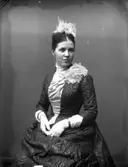 Porträtt av Mathilda Ranch, sittande i elegant klänning, vita handskar samt hår- och axeldekor.
(Se även MR2_2459 och MR3_2600)