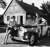 En kvinna och en man står vid en DKW Meisterklasse årsmodell 1937. Bilden tagen i Skåne år 1951. I bakgrunden Kullens mejeri.