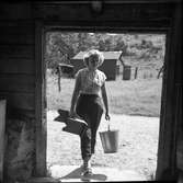 Ingela Öberg med mjölkspann och mjölkpall på väg in genom dörren till ladugården.