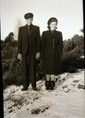 Karl och Anna Snygg står finklädda i lätt snöig terräng med enebuskar.