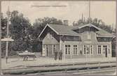 Spårsida av station med vy på stationshus och perrong med personal.