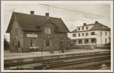 Spårsida av station med vy på stationshus med byggnad i bakgrunden.