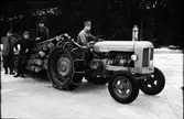Traktor försedd med snökedjor drar ett timmerlass över isen. På traktorn (en Fordson Major) sitter Börs-Bengt Eriksson och mannen längst till vänster är John Johnsson, 