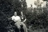 Rune Engström (1921 - 2007) sitter på en bänk bredvid modern Elsa Engström (1892 - 1983). De bodde i lägenhet i ett uthus tillhörande Vommedal Östergård 