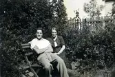 Rune Engström (1921 - 2007) sitter på en bänk bredvid modern Elsa Engström (1892 - 1983) cirka 1940. De bodde i lägenhet i ett uthus tillhörande Vommedal Östergård 