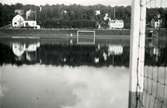 Ca. 1949 fotbollsplan på Kärret, vattendränkt.
I bakgrunden Kyrkbacken, t. v. Henrikssons affär.
Bakom trädhäcken byggdes på 1950-talet prästgården. 
T. h. Villa Solliden.