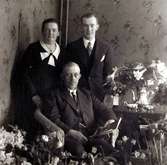 Tre okända personer varav en sitter på en stol om given av blommor-