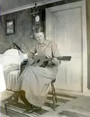 Esther Jakobsson spelar gitarr inne i boningshuset Lilla Vommedal (idag: Streteredsvägen 25), 1913-08-10. Esther var fosterdotter till Anton och Maria Gustafsson. Ägare av Lilla Vommedal. Syster till Oscar Jakobsson (1889-1945), skaparen av den folkkäre seriefiguren Adamson. Esther avled i TBC 1926.
