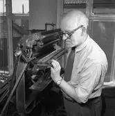 Arboga Tidning, personal och interiör.
En man, iklädd skjorta och slips, arbetar vid en maskin. Utsikten genom fönstret visar, att lokalen ligger någon våning upp i huset.