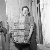 Arboga Tidning, personal och interiör.
En ung man står, i dörröppningen, med flera tidningsbuntar i famnen.