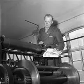 Arboga Tidning, personal och interiör.
En man inspekterar tryckpressen. Han är iklädd skyddsrock och håller en tidning i handen.