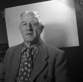 Arboga Tidning, personal. Porträttbild av man med kavaj och slips. 
Fotografens assistent håller upp en vit bakgrund.