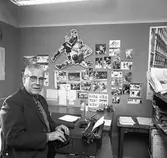Arboga Tidning, personal och interiör. En man sitter vid skrivmaskinen. Han är förmodligen sportjournalist. På väggen sitter en stor samling idrottsfotografier. I bokhyllan, framför mannen, står en skrift med titeln 
