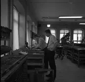 Arboga Tidning, personal och interiör.
Flera personer arbetar i lokalen. Fack med typer ses i förgrunden. En man bygger en tidningssida.