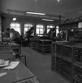 Arboga Tidning, personal och interiör. Sex män arbetar i rummet. Männen till vänster bygger tidningssidor med typer. Längst bort i lokalen står tre maskiner. Arbetsbord och skåp med lådor ses i bilden.