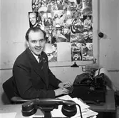 Arboga Tidning, personal och interiör. Journalisten Rune Ström vid skrivmaskinen. På väggen bredvid sitter diverse foton. I förgrunden syns en telefon.