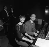 Arbogabor närvarar vid sändningen av Frukostklubben, ett underhållningsprogram som sänds på lördagsmorgnar. En kvinna och en man spelar fyrhändigt på pianot.