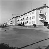 Flerfamiljshus i Vasastaden. Porten på gavlen har adress Stationsgatan 2.
Längre bort på gatan syns en kvinna och en bil.