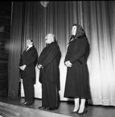 Arbogarevyns medlemmar spelar upp sin Jubileumsrevy. Tre personer står på scenen, två klädda i frack och den tredje i kappa och sjalett.